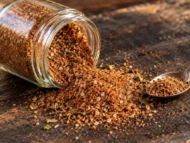 Cajun-inspired blackening rub spilling from a glass jar onto dark wood