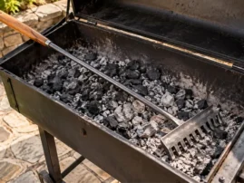 Long-handled charcoal rake resting in the coal bed of a charcoal grill