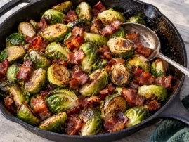 Grilled Brussels sprouts with browned edges and crisp bacon pieces in a cast-iron skillet.