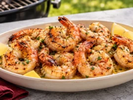 Grilled shrimp coated in garlic butter and parsley with lemon wedges on a serving platter.