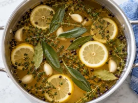 Prepared turkey brine with lemon slices, sage, thyme and peppercorns in a food-safe vessel.