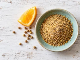 Orange coriander turkey rub in a blue bowl with an orange wedge and coriander seeds