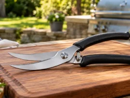 Poultry shears with black handles resting on a wooden cutting board outdoors