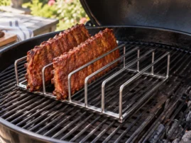 Two slabs of ribs standing upright in a metal rib rack inside a kettle grill