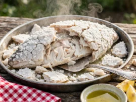 Salt-crusted whole sea bass with the crust cracked open, a vintage silver pie server lifting the first fillet, lemon wedges beside.