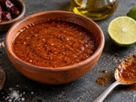 Rustic bowl of smoky chipotle lime marinade with dried chipotle peppers, garlic and halved limes beside it